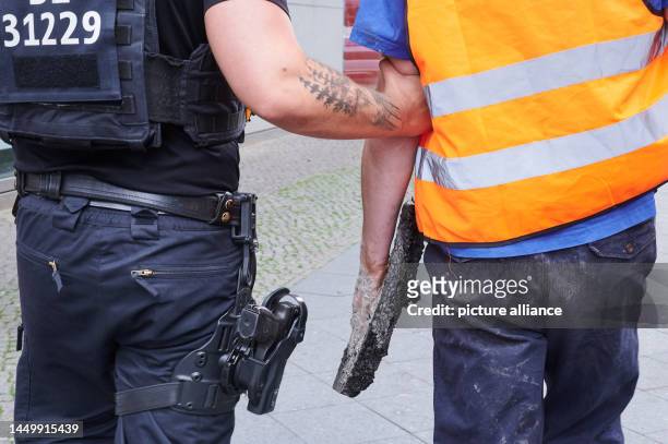 Police lead an activist of the climate protection group Letzte Generation off the street with asphalt still hanging from his hand. Last Generation...