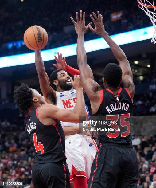 Kyrie Irving of the Brooklyn Nets goes to the basket against Christian Koloko and Scottie Barnes of the Toronto Raptors during the first half of...