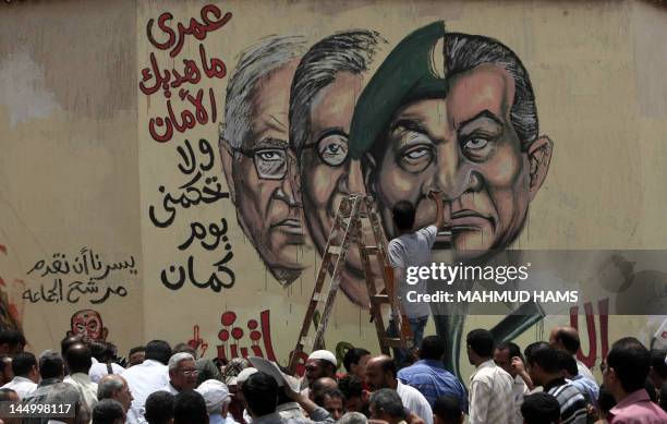 Man puts the finishing touches on graffiti picturing the morphed faces of Egyptian ousted president Hosni Mubarak and military ruler Hussein Tantawi...