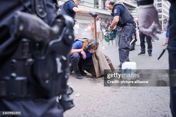 An activist of the climate protection group Letzte Generation sticks his hand on Friedrichstraße while police officers come with circular saw and...