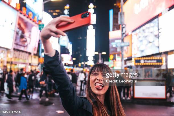 glückliche frau macht ein selfie auf dem times square, um es in den sozialen medien zu teilen - times square night stock-fotos und bilder