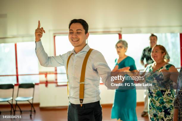 jovem instrutor de dança dando uma aula para um grupo de estudantes maduros em um estúdio de dança - instructions - fotografias e filmes do acervo