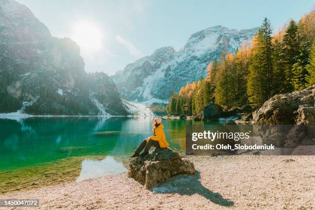 frau sitzt im winter auf dem hintergrund des pragser wildsees - yellow coat stock-fotos und bilder