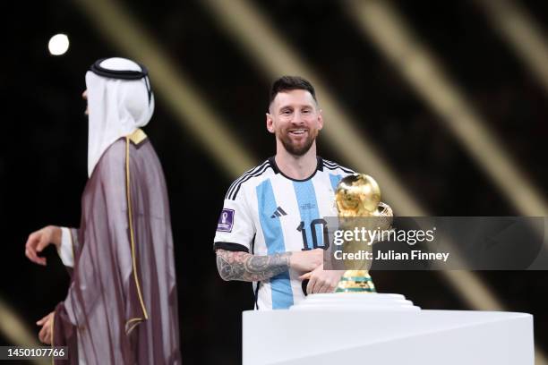 Lionel Messi of Argentina looks at the FIFA World Cup Qatar 2022 Winner's Trophy while holding the adidas Golden Boot award after the FIFA World Cup...