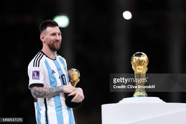 Lionel Messi of Argentina looks at the FIFA World Cup Qatar 2022 Winners' Trophy while holding the adidas Golden Boot award after the FIFA World Cup...
