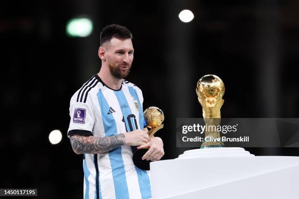 Lionel Messi of Argentina looks at the FIFA World Cup Qatar 2022 Winners' Trophy while holding the adidas Golden Boot award after the FIFA World Cup...