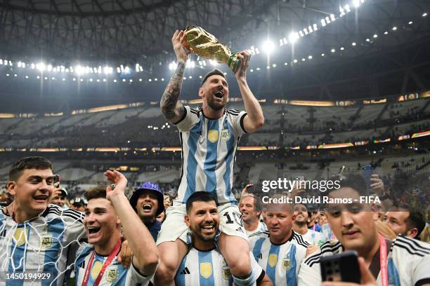 Lionel Messi of Argentina celebrates with the FIFA World Cup Qatar 2022 Winner's Trophy on Sergio 'Kun' Aguero's shoulders after the team's victory...