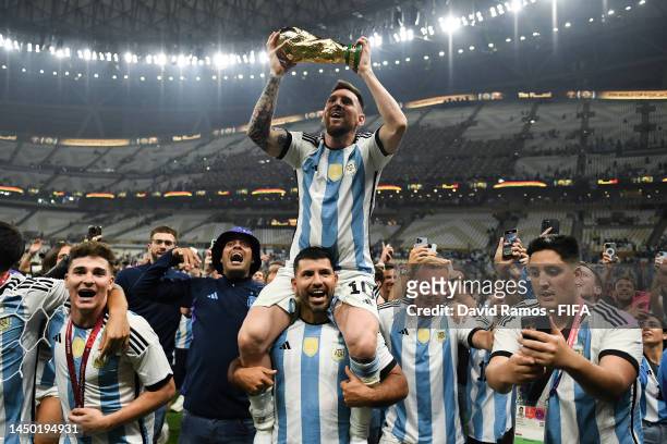 Lionel Messi of Argentina celebrates with the FIFA World Cup Qatar 2022 Winner's Trophy on Sergio 'Kun' Aguero's shoulders after the team's victory...
