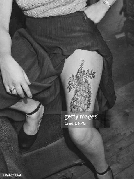 Woman hitches up her skirt to reveal a large tattoo of a peacock on her thigh, Copenhagen, Denmark, circa 1945.