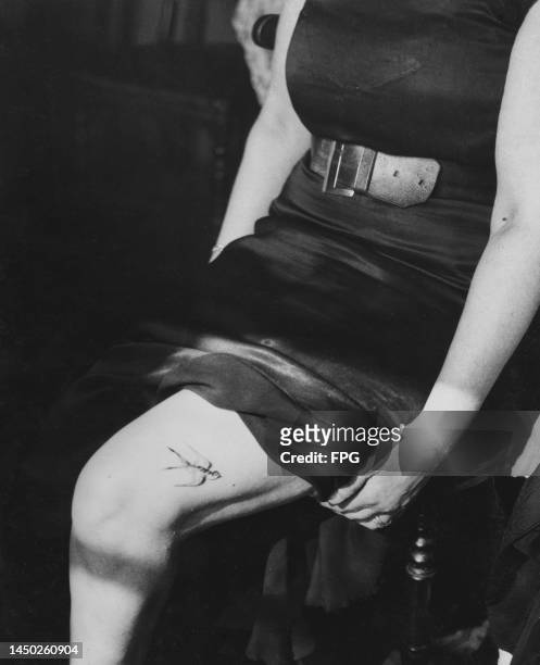 Woman hitches up her skirt to reveal a tattoo of a swallow on her thigh, London, England, circa 1935.