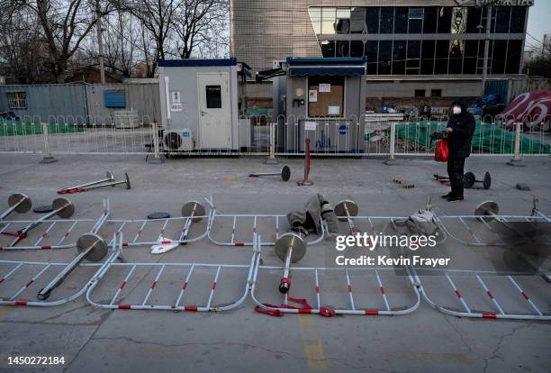 Woman walks by barricades as they are seen scattered on the ground at a nucleic acid testing site for COVID-19 that is still operating on December...