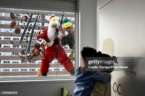 Santa Claus greets a child in the hospital to give her a present as he hangs on the facade of the Germans Trias i Pujol University Hospital , on 19...