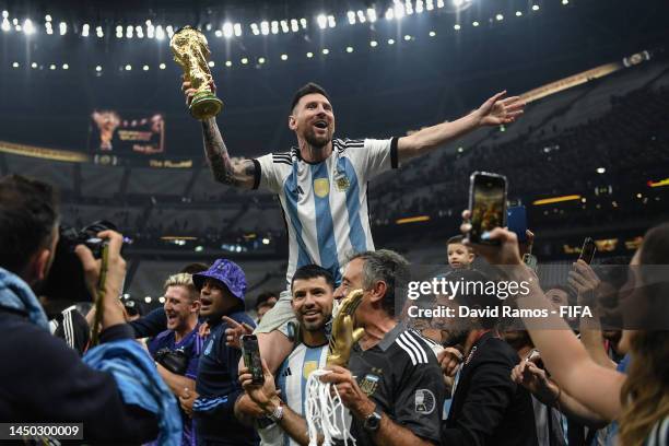 Lionel Messi of Argentina celebrates with the FIFA World Cup Qatar 2022 Winner's Trophy on Sergio 'Kun' Aguero's shoulders after the team's victory...