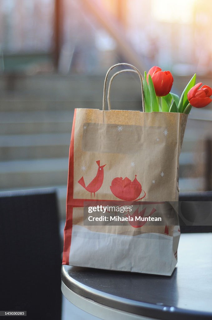 Two red tulips in paper bag on table at sunset