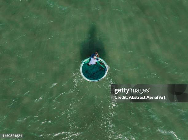 drone shot looking down on a lone fisherman in a circular shaped fishing vessel on a sunny day, vietnam - minimal effort stock pictures, royalty-free photos & images