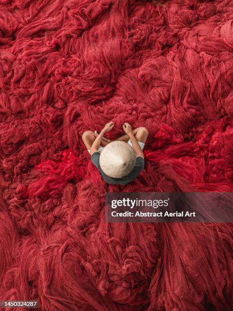 drone image directly above a fisherman wearing a conical hat repairing a red coloured commercial fishing net, vietnam - fibre stock pictures, royalty-free photos & images