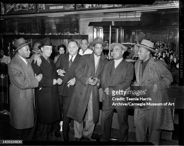 Portrait of a group of men, including businessman and baseball team owner Gus Greenlee and bartender Tom West as they pose at the bar in the Crawford...