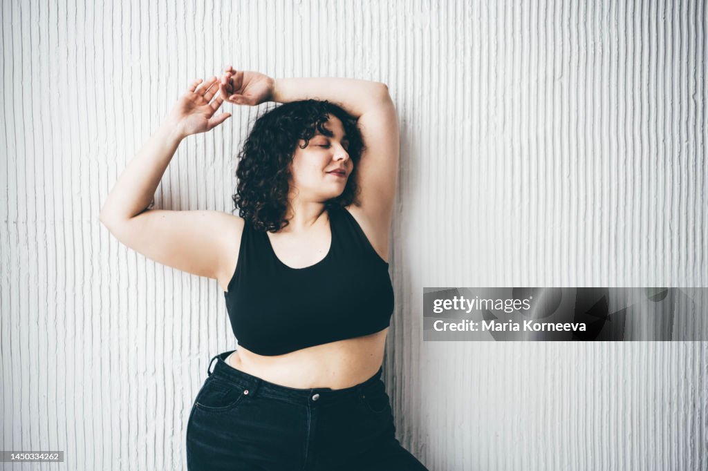 Cheerful plus size woman standing against wall.