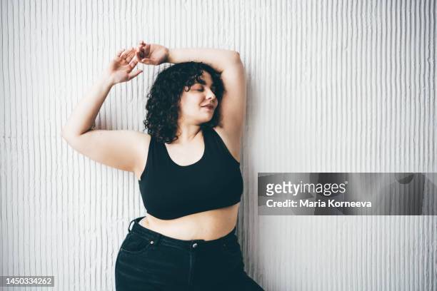 cheerful plus size woman  standing against wall. - curvy woman stock-fotos und bilder