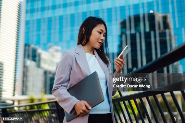 young asian businesswoman with laptop, using smartphone against financial buildings in the city - banking stock pictures, royalty-free photos & images