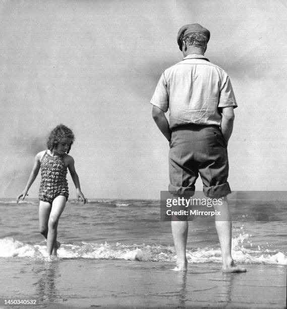 The picture shows a father or grandfather with a little girl on the beach. They both have their feet in the water. July 1952.