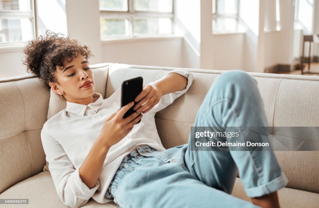 Business woman, couch and phone while browsing and relaxing at home after a work day. Text, text message and internet scrolling with a girl relaxing and searching social media for contact