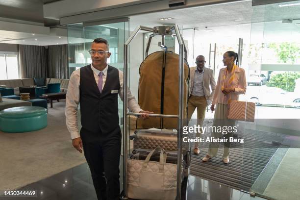 couple arriving at a luxury hotel assisted by the porter - porter stock pictures, royalty-free photos & images