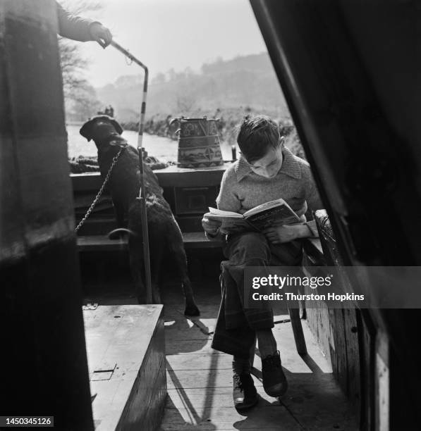 Boy reading his book sitting on a barge on the Grand Union Canal, England. Original Publication: Picture Post - 7798 - The Scandal of our Waterways -...