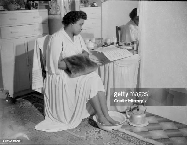 Winifred Atwell, pianist, puts her feet into bowl of hot water and her hands in a muff to overcome the cold. 12th February 1951.