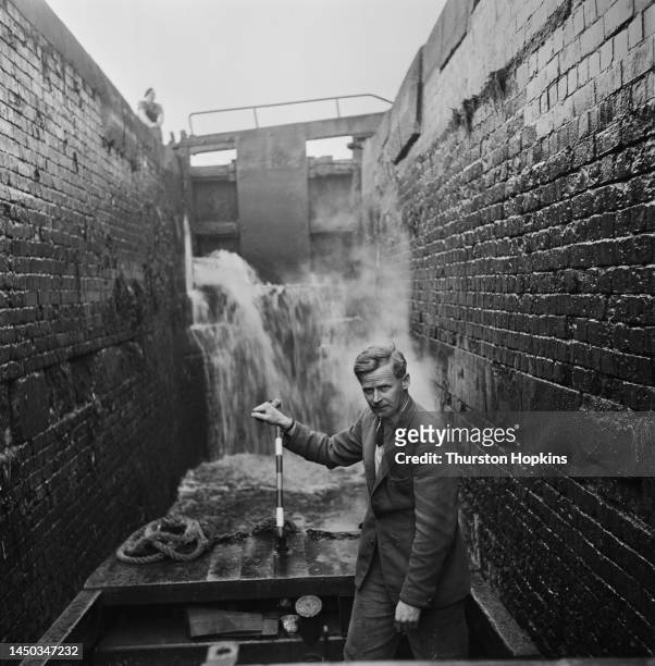Man operates the tiller of a narrow boat moving through a lock on the Grand Union Canal, England. Original Publication: Picture Post - 7798 - The...