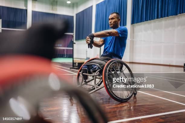 disabled asian man in wheelchair putting on uniform and checking safety before going to badminton court. - badminton sport stockfoto's en -beelden
