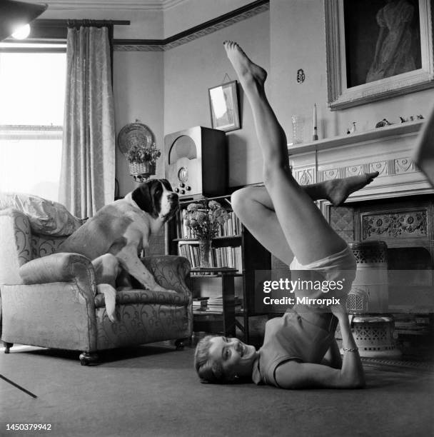 Shirley Burke stretching in the living room of her home with her pet St. Bernard Dog watching. October 1952.