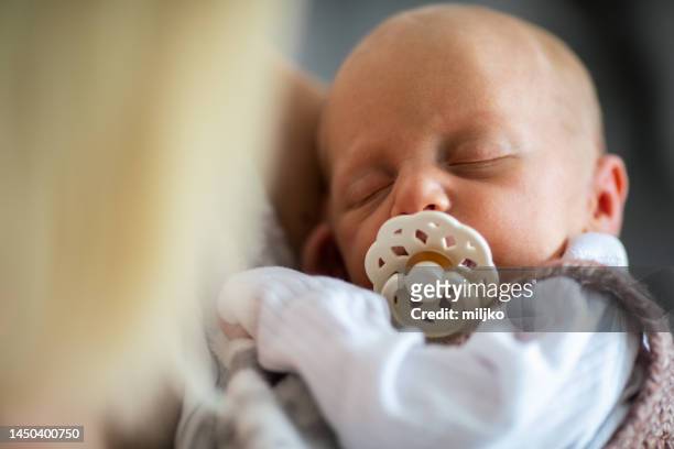 newborn baby sleeping in her mother's arms - pacifier stockfoto's en -beelden