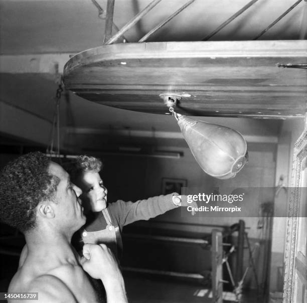 Boxer Alex Buxton seen here holding his son, using a punchball during a training session . May 1953.