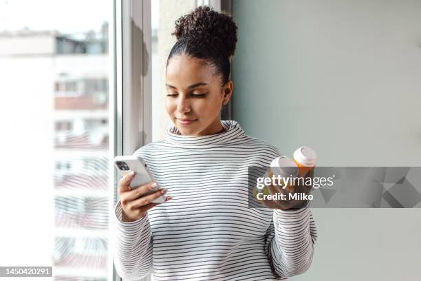 eine junge, glückliche frau mit einem smartphone und einer pillenflasche - treatment stock-fotos und bilder