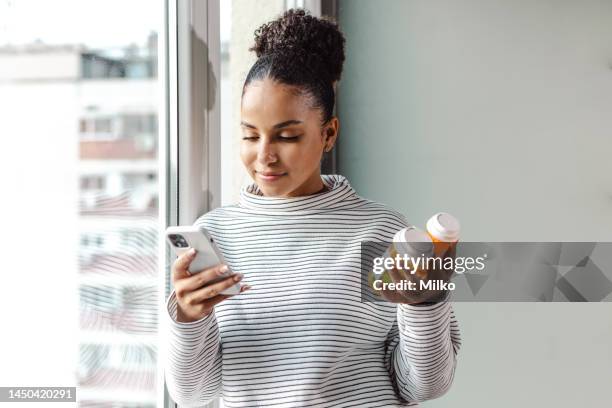 a young happy woman holding a smart phone and a pill bottle - prescription imagens e fotografias de stock
