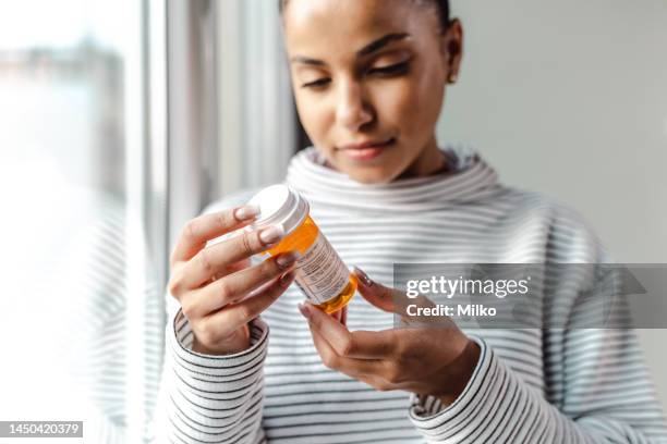 una giovane donna seria che tiene in mano una bottiglia di medicine - prendere-le-medicine foto e immagini stock