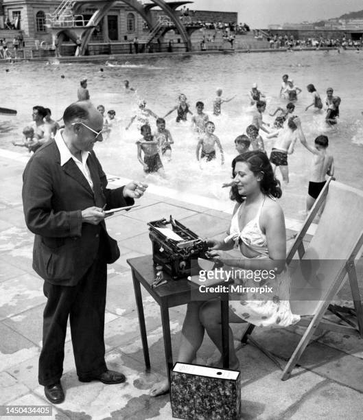 Woman typist working in the sun beside a swimming pool filled with children having fun and splashing the water around. While her manager dictates a...