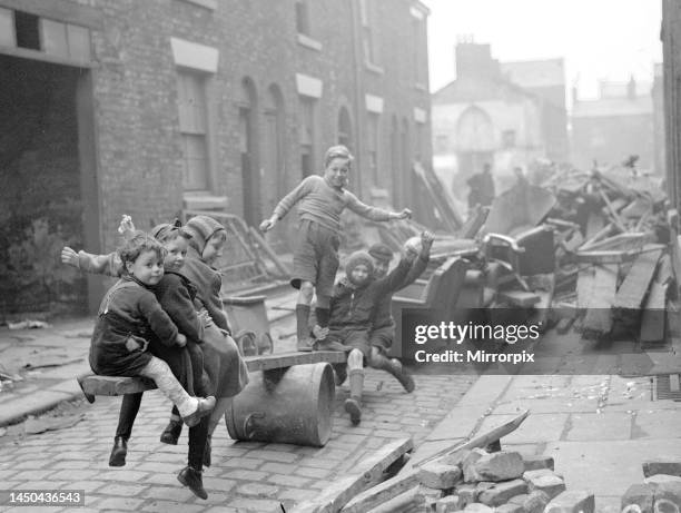 Children make a see-saw out of an upturned dustbin and a plank of wood in a street full of debris after a bomb raid in London. September 1940.