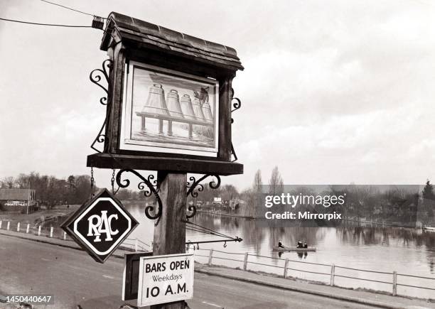 The pub sign outside The Bells of Buzeley pub in Windsor, Berkshire. In the background two men row on the river. Circa 1950.