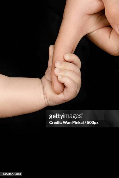 the baby holds the parents' fingers in the black background - xiaogan stock pictures, royalty-free photos & images