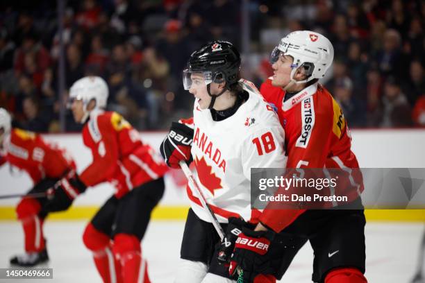 Cedar Bankier# 18 team Canada gets held onto by Nick Merle of Switzerland in during the 2023 IIHF World Junior Championship game at Avenir Centre on...