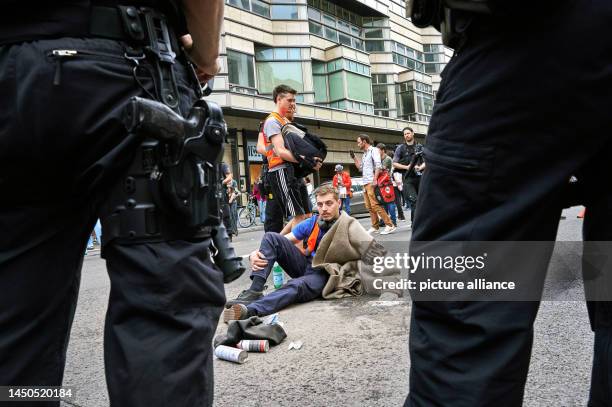 An activist of the climate protection group Letzte Generation sticks his hand on Friedrichstraße while police officers stand around him. Last...