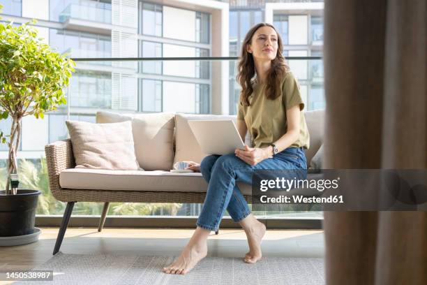 thoughtful businesswoman with laptop on sofa at home - arabian gulf cup stock pictures, royalty-free photos & images