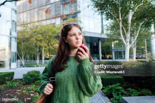 thoughtful young woman eating apple in front of building - apple products stock pictures, royalty-free photos & images