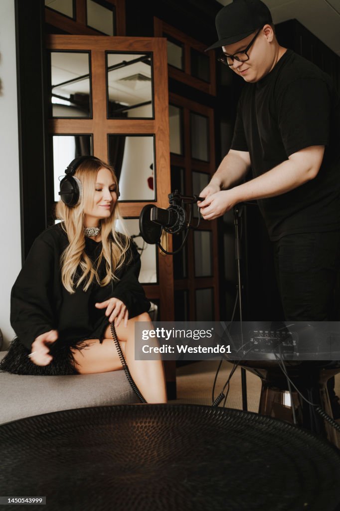 Smiling musician recording podcast through microphone held by colleague in studio