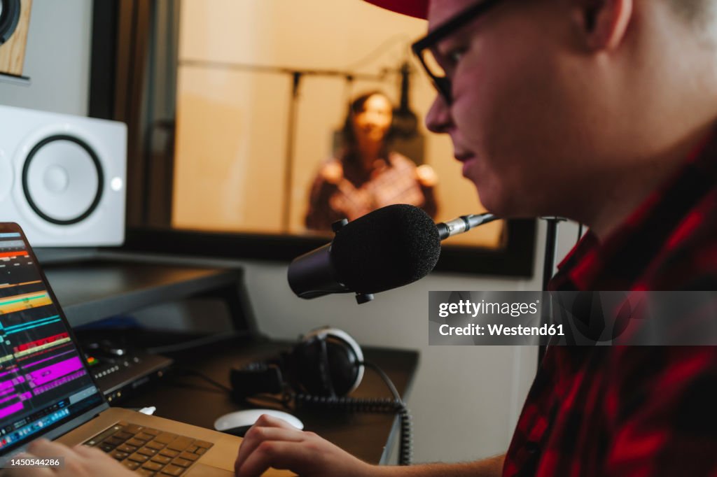 Sound engineer composing on laptop with singer in background at recording studio