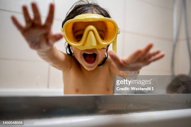cheerful boy wearing swimming goggles taking bath in bathroom at home - incidental people stock pictures, royalty-free photos & images
