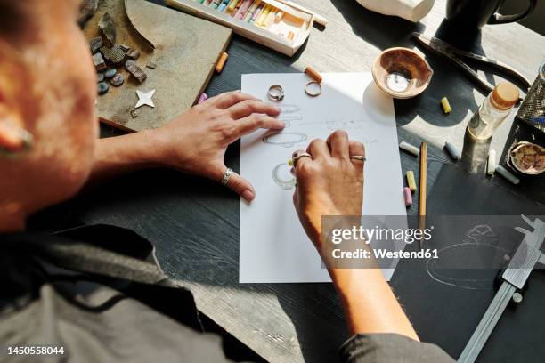 jeweller sketching ring design on paper at workbench - juwelier stockfoto's en -beelden