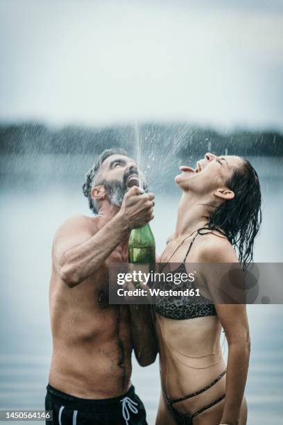 cheerful couple celebrating with champagne in lake - spraying champagne stock pictures, royalty-free photos & images